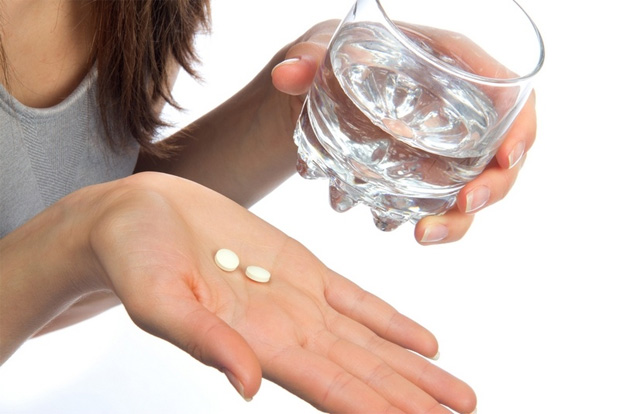 Девушка держит на ладони две таблетки и другой рукой стакан воды