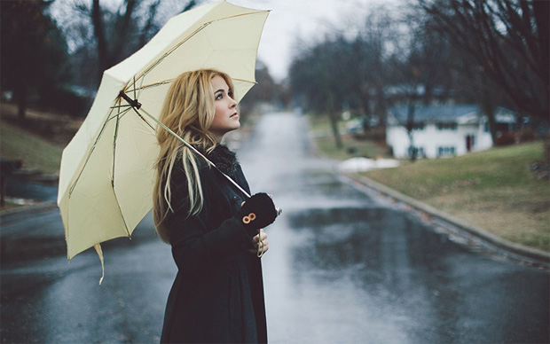 Девушка на улице стоит под большим бежевым зонтиком