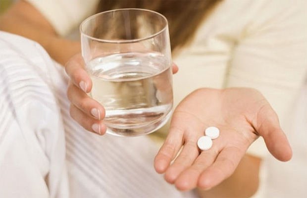 Девушка со стаканом воды в руках держит на ладони две таблетки