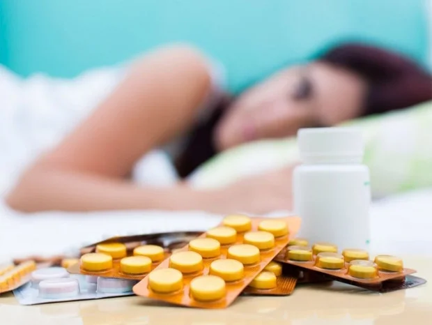 Девушка лежит на кровати, а перед ней разные лекарства