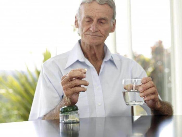 Пожилой мужчина за столом держит лекарство и стакан воды