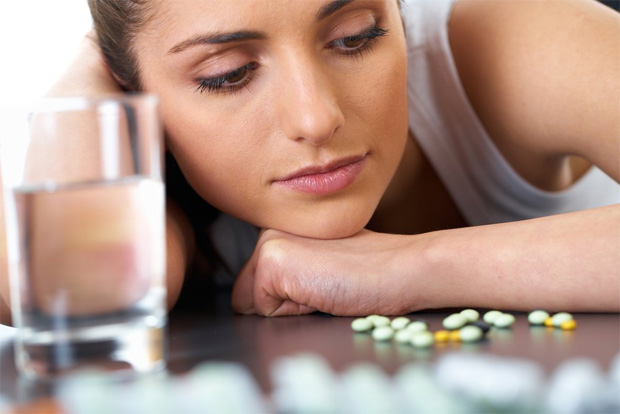 Девушка со стаканом воды смотрит на горсть лекарств