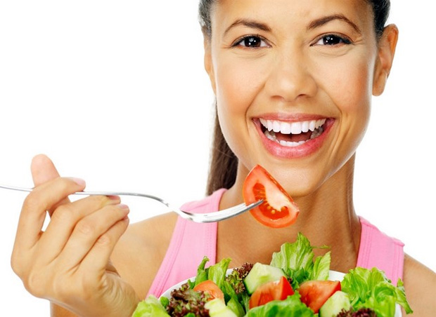 Улыбающаяся девушка ест салат из свежих овощей