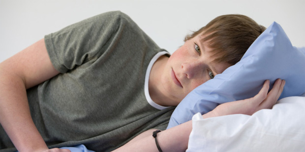 Молодой подросток лежит на кровати с грустным видом