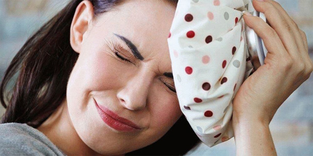 Девушка с сильной головной болью прикладывает ко лбу холодный компресс