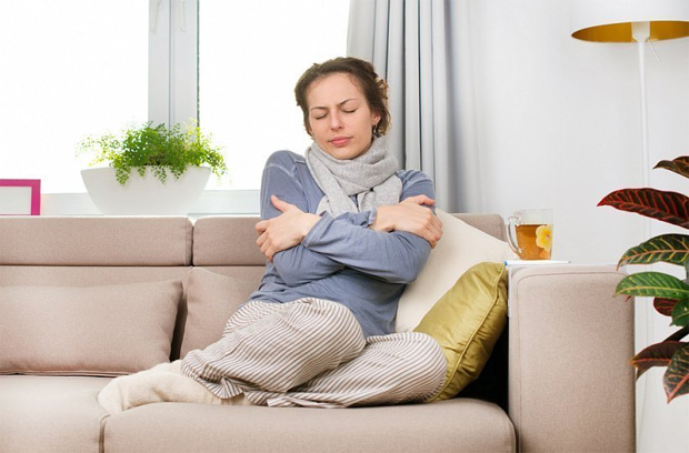 Женщина в теплой одежде сидит на диване дома и мерзнет