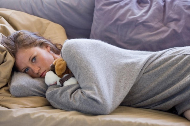 Девушка лежит дома на диване, обняв мягкую игрушку