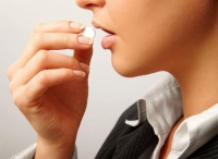 Девушка кладет в рот большую таблетку для устранения недуга